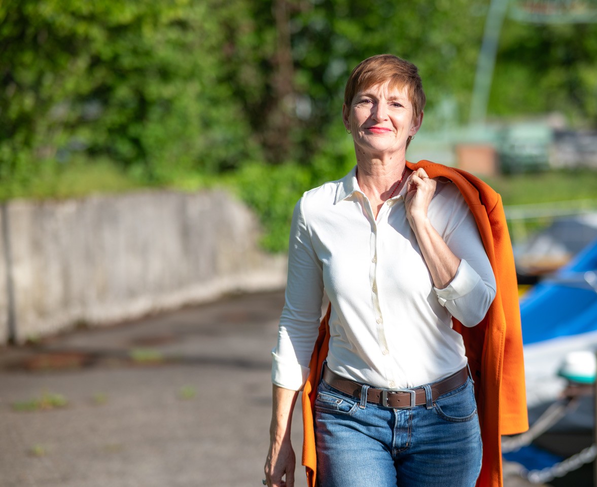 Barbara Mieg walking outdoors, an orange coat over her shoulder