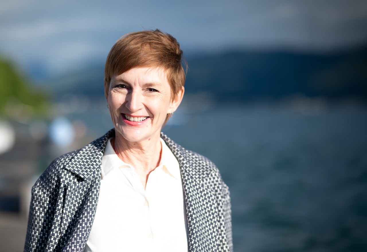 Barbara Mieg smiling by the lake, a patterned jacket over a white blouse